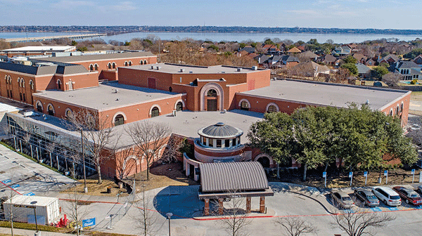 Pecos County Memorial Hospital - Texas Hospital Association A large brick educational campus building with a circular entrance, surrounding parking, trees, and a body of water in the background.
