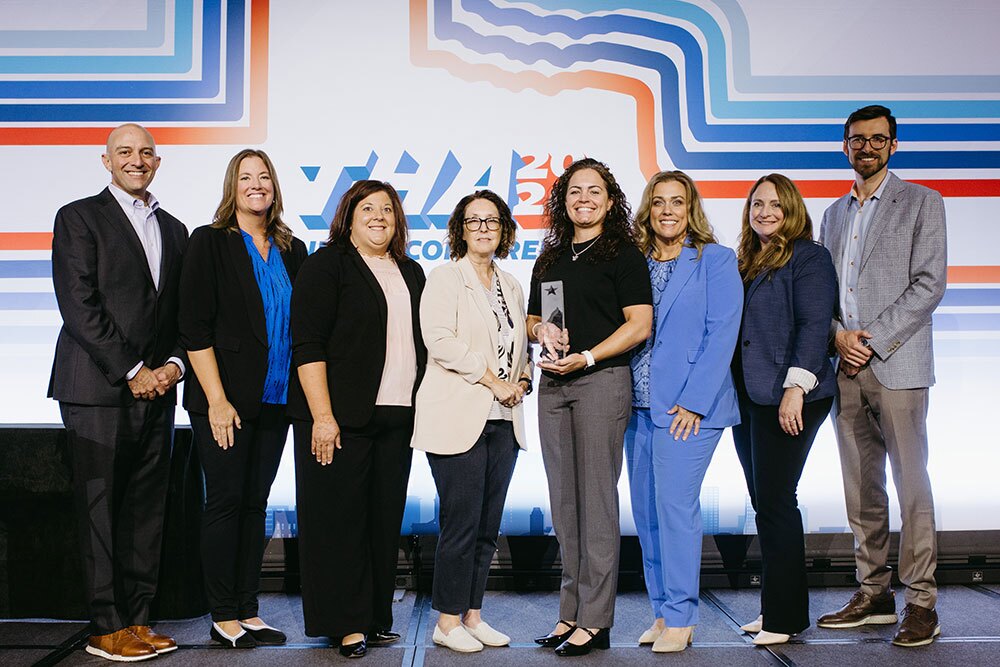 Baylor Scott & White Medical Center – Grapevine accepting the Bill Aston Award for Quality, Academic Institution or Large Teaching Hospital or Health System - Texas Hospital Association Group of eight professionals on stage posing with a glass award against a colorful backdrop at a conference.
