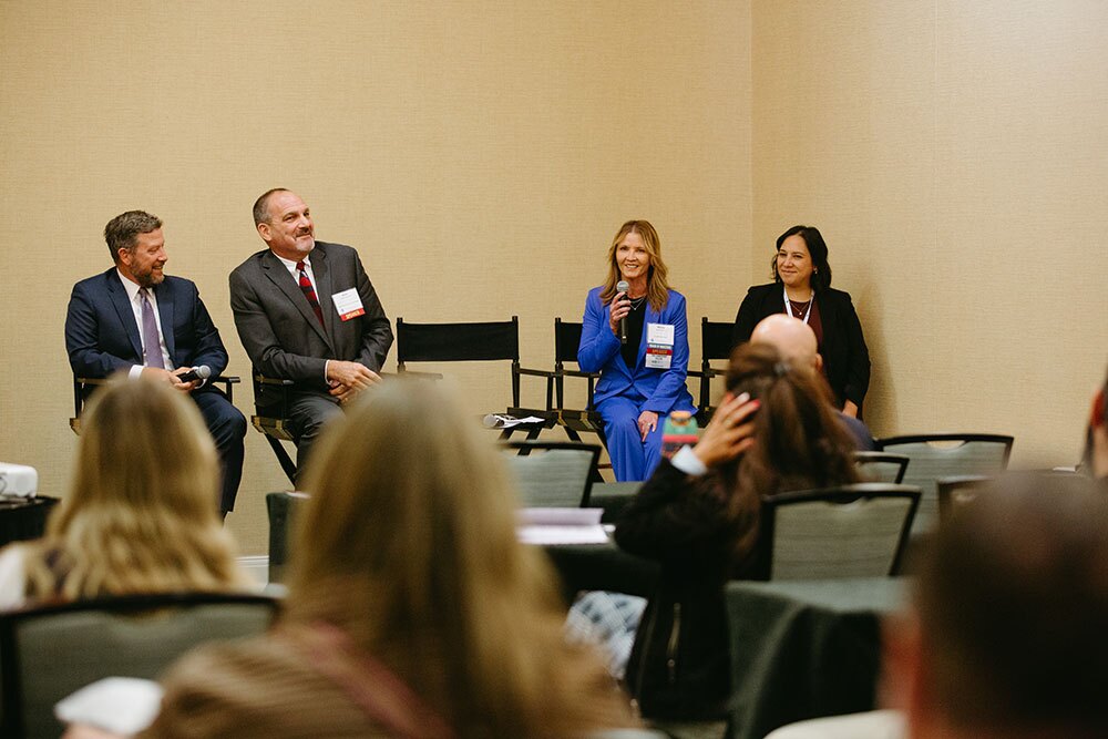 A panel of behavioral healthcare leaders lead a breakout session around gaps in care and the partnerships needed - Texas Hospital Association Panel of four professionals seated on a stage at a conference, woman in blue speaking into a microphone while others listen and audience watches.