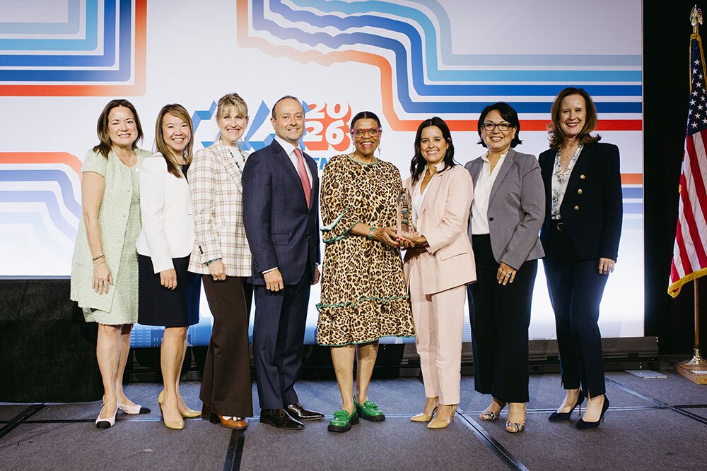 Excellence in Community Service Award winners from Texas Health Resources - Texas Hospital Association Group of eight professionals on a stage posing for a formal event photo, with geometric backdrop and an American flag on the right core image.
