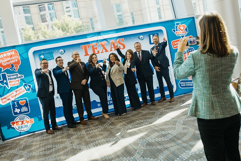 THA's 2026 Class of Leadership Fellows reconnected and presented capstone projects during the conference - Texas Hospital Association Group of professionals posing for a photo in front of a Texas Hospitals banner; a person in foreground takes their picture.