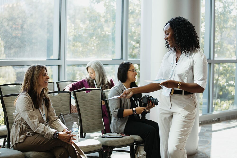 Conference attendees learned about THA programs and services - Texas Hospital Association Professional woman standing and handing a document to seated colleagues in a bright conference room.