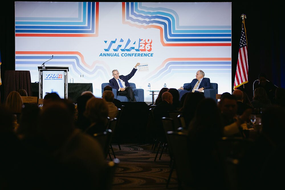 THA President/CEO John Hawkins (right) joined outgoing American Hospital Association President and CEO Rick Pollack for a fireside chat - Texas Hospital Association Two men sit on a conference stage in discussion, one gesturing with an arm raised; a bold banner reads'Annual Conference 2026' and a US flag stands to the side as the audience watches.