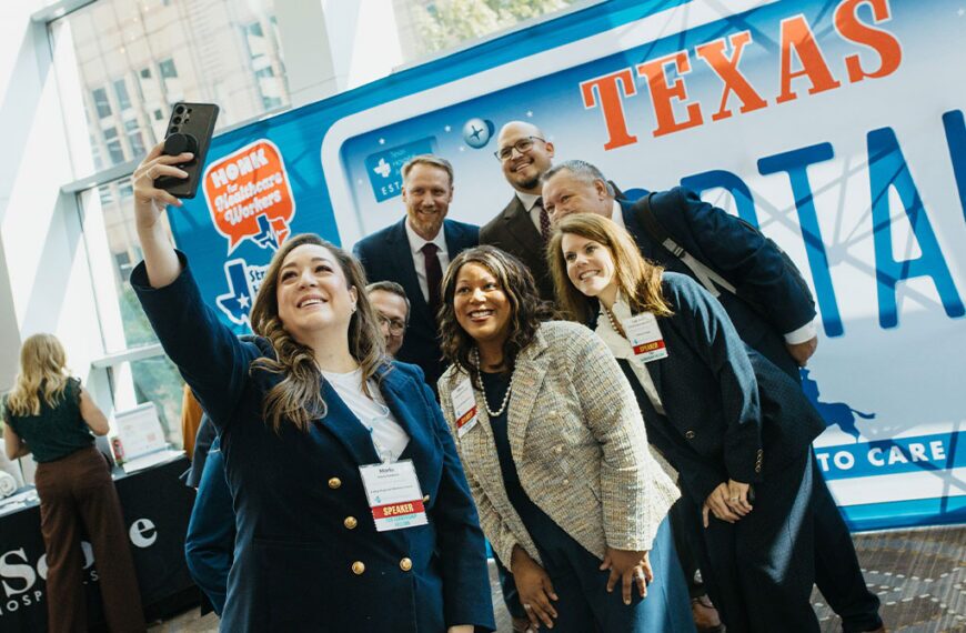 Diverse professionals posing for a selfie at a healthcare event, badges visible, in front of a blue Texas-themed bus.