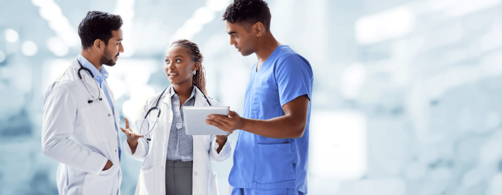 Peer Review Network - Texas Hospital Association Three clinicians in a hospital hallway discuss a tablet; two wear white coats with stethoscopes and one wears blue scrubs.