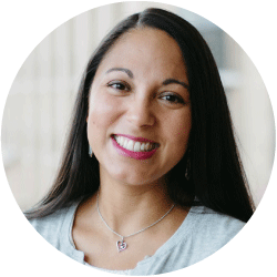 Nina-Costilla-926 - Texas Hospital Association Portrait of a smiling woman with long dark hair, wearing a light blue top and a heart-shaped pendant necklace in a circular crop.