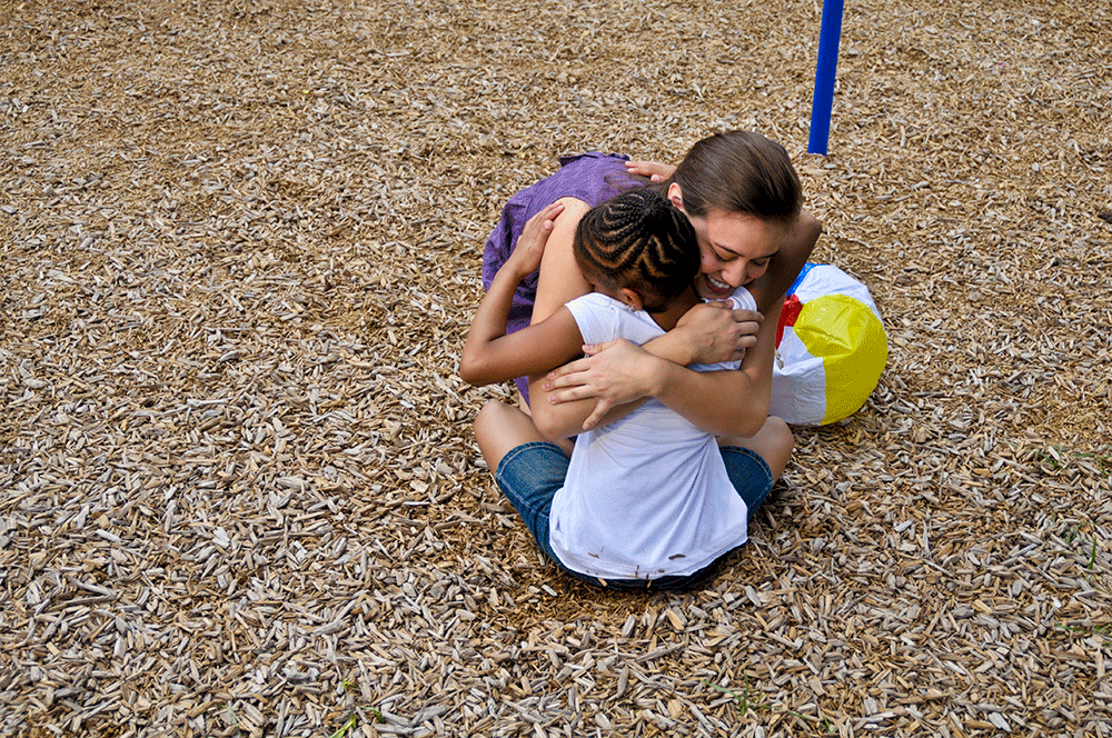 Hospital Week: Clarity Child Guidance Center - Texas Hospital Association Two children share a warm hug on a wood-chip playground surface, with a colorful beach ball nearby.