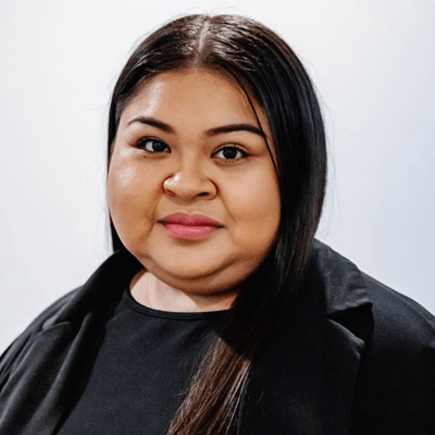 Portrait of a woman with long dark hair wearing a black top and blazer against a light background, looking at the camera with a subtle smile.