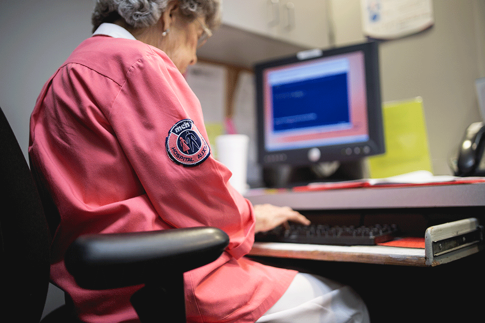 The Vital Role of Volunteers in Texas Hospitals - Deskwork - Texas Hospital Association A hospital volunteer sitting at a desk and entering form data on a computer keyboard.