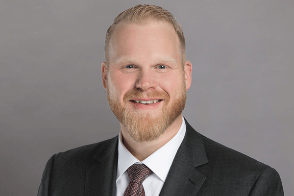 Adam Willmann - Texas Hospital Association Professional headshot of a smiling man in a dark suit and white shirt against a gray backdrop.
