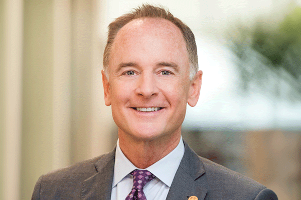 Allen Harrison - Texas Hospital Association Smiling middle-aged man in a gray suit and purple tie, posing for a professional headshot with a blurred office background.