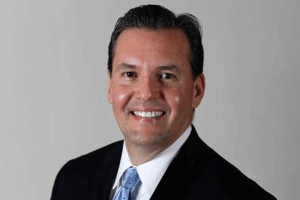 Edmundo Castaneda - Texas Hospital Association Professional headshot of a smiling man in a dark suit and blue tie against a neutral gray background.