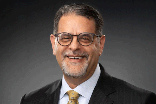 Jim Parisi - Texas Hospital Association Smiling man in a dark suit and yellow tie, wearing glasses in a professional headshot.