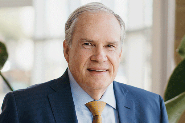 John Hawkins - Texas Hospital Association Portrait of a middle-aged man in a navy suit and yellow tie, smiling in a bright office setting.