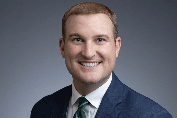 Lance Ames - Texas Hospital Association Professional headshot of a smiling man in a blue suit, white shirt, and green tie against a gray backdrop.