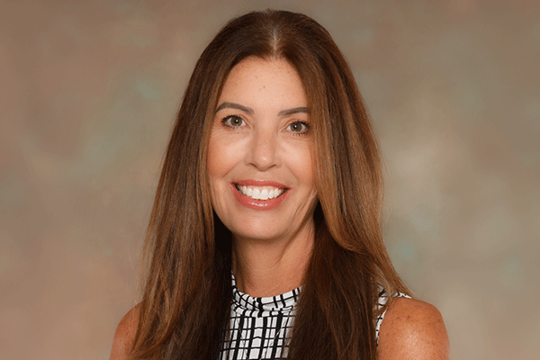 Lori Boyd - Texas Hospital Association Portrait of a smiling woman with long brown hair wearing a black-and-white patterned sleeveless top against a neutral backdrop
