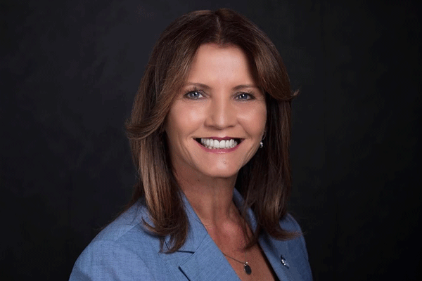 Marie Alvarez - Texas Hospital Association Professional portrait of a smiling woman with shoulder-length brown hair wearing a blue blazer against a dark background.