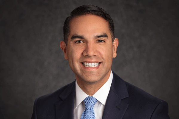Nicholas Tejeda - Texas Hospital Association Professional headshot of a smiling man in a dark suit and blue tie against a neutral backdrop.