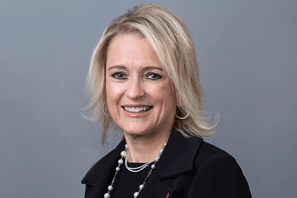Pam Stoyanoff - Texas Hospital Association Professional woman with shoulder-length blonde hair, wearing a black blazer and pearl jewelry, smiling against a gray studio background.