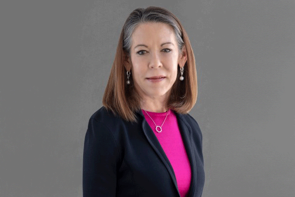 Susan Turley- - Texas Hospital Association Professional head-and-shoulders portrait of a middle-aged woman in a navy blazer and pink blouse, against a gray background.