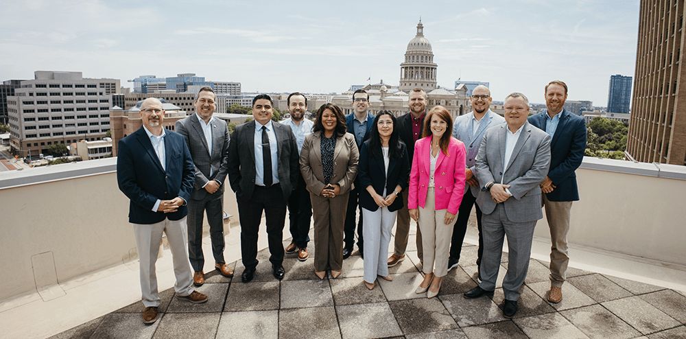 THA Leadership Fellows Class of 2026 - Texas Hospital Association Twelve professionals posing on a rooftop with a city skyline and domed capitol building in the background.