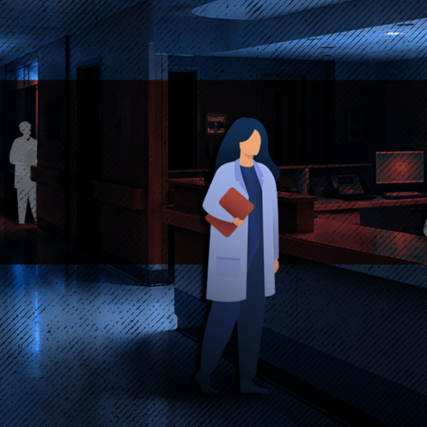 Healthcare worker in a blue coat holding a folder, standing in a dim hospital hallway.