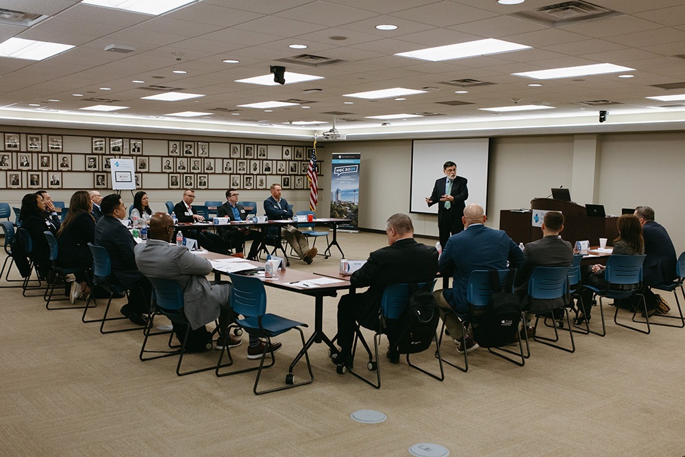 THA Fellows Class of 2026 at work - Texas Hospital Association Business meeting in a large conference room with attendees seated around a U-shaped table and a presenter at the front near a projector screen and American flag/portrait wall behind them.