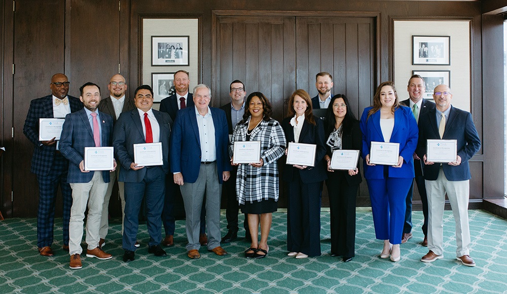 THA Fellows Class of 2026 presenting their graduation certificates - Texas Hospital Association Group of diverse professionals posing in a formal room, each holding a certificate of achievement.