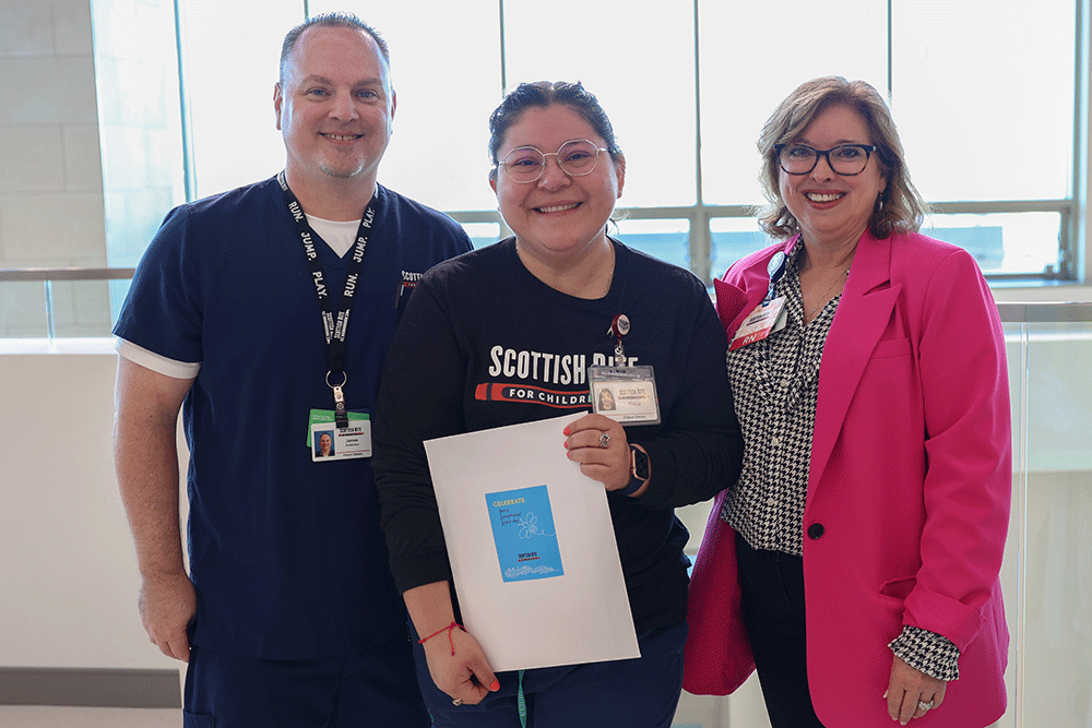 Angie Buckmeier, right - Texas Hospital Association Three healthcare workers pose together in a bright hallway; center person holds a document or folder with a blue cover.