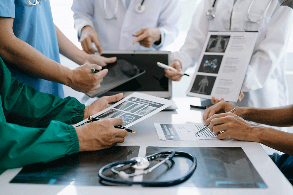 Medical team reviews X-ray images and charts on a table during a clinical meeting, stethoscope nearby