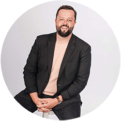 Ryan Campbell - Texas Hospital Association Smiling man in a black blazer and beige sweater sits against a light backdrop.