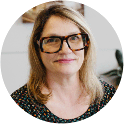 Head-and-shoulders portrait of a smiling woman with blonde hair and black rectangular glasses, circle crop.