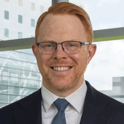 Brad Nitschke - Texas Hospital Association Professional headshot of a smiling man in a dark suit and blue tie, wearing glasses, in an office backdrop.