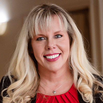 Candice Smith - Texas Hospital Association Smiling woman with long blonde hair and bangs, wearing a red blouse and black blazer, indoors.