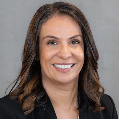 Sandi Gill - Texas Hospital Association Professional headshot of a smiling woman with dark brown hair, wearing a black blazer against a gray backdrop.