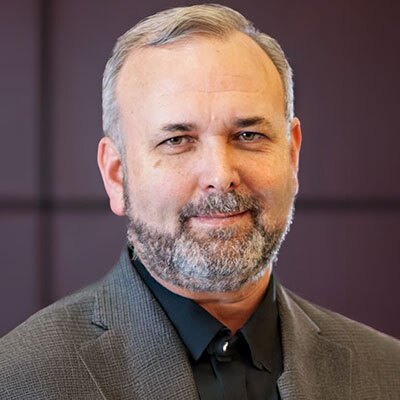 Terry-Scoggin-2026 - Texas Hospital Association Portrait of a middle-aged man with gray hair and beard, wearing a dark shirt and gray blazer.