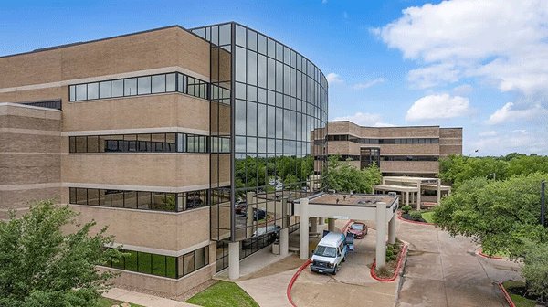 CHI St. Joseph Health - College Station Hospital - Texas Hospital Association Modern office building with a curved glass atrium, brick wings, and a driveway with two vans at the entrance.