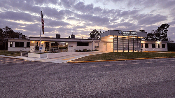 Chambers Health - Texas Hospital Association Exterior of Chambers Health clinic at dusk, single-story building with flagpole, ramp, and illuminated sign reading'Chambers Health.'
