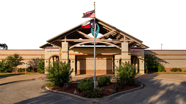 Yoakum Community Hospital - Texas Hospital Association Front view of a brick public building with a flagpole and flags in a circular driveway area.