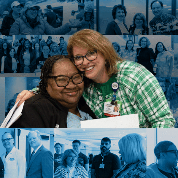 Two smiling women hug in the foreground at a conference, with a blue-tinted collage of team photos behind them.